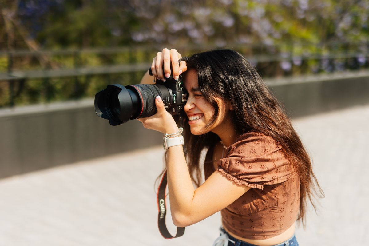 Joven creadora de contenido sonriente capturando un momento al aire libre con su cámara DSLR